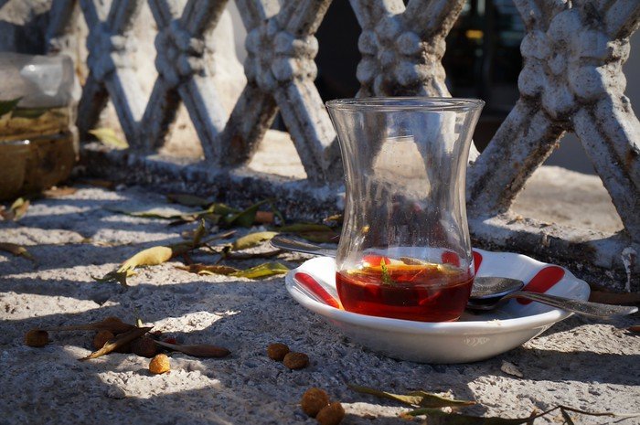 A traditional tulip-shaped glass of rich Turkish tea resting on a saucer with a spoon, set on a sunlit stone ledge along the streets of Istanbul, Turkey, capturing a quiet everyday moment