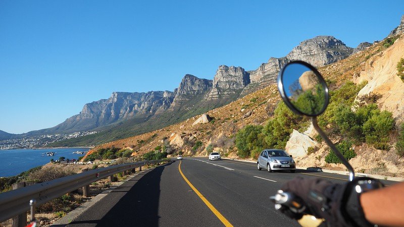 Scenic view of the Twelve Apostles mountain range along Cape Town’s Atlantic Seaboard, captured from a sidecar motorcycle ride during a Cape Peninsula tour, with winding coastal road, clear blue skies, rugged cliffs, and the ocean glistening below