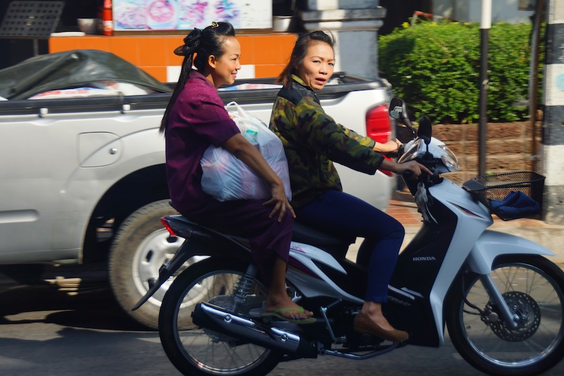 Two ladies riding the same scooter carrying items without helmets in SE Asia Two ladies riding the same scooter carrying items without helmets in SE Asia