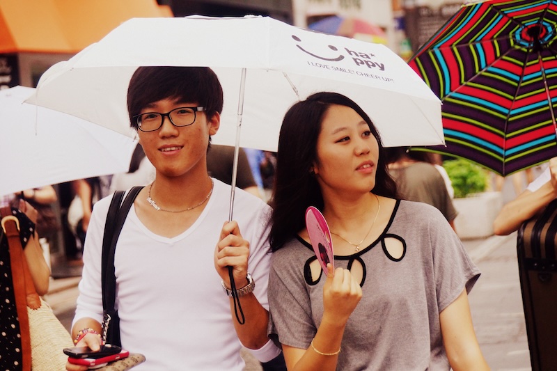 Typical Seoul summer street scene with couple using sun umbrellas 