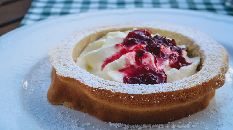 Tyrolean desserts to try - Prügeltorte which is a cake cooked on a cylinder over a fire and is topped with cream and berries and icing sugar