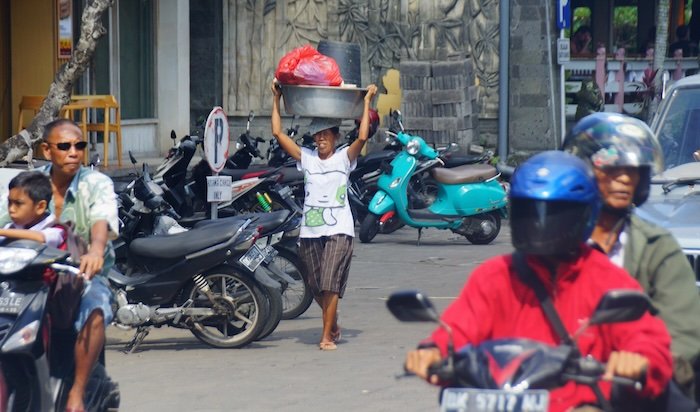 Ubud lady carrying a pan on her head in the background and scooters buzzing around in the foreground backpacking around Bali, Indonesia in SE Asia 
