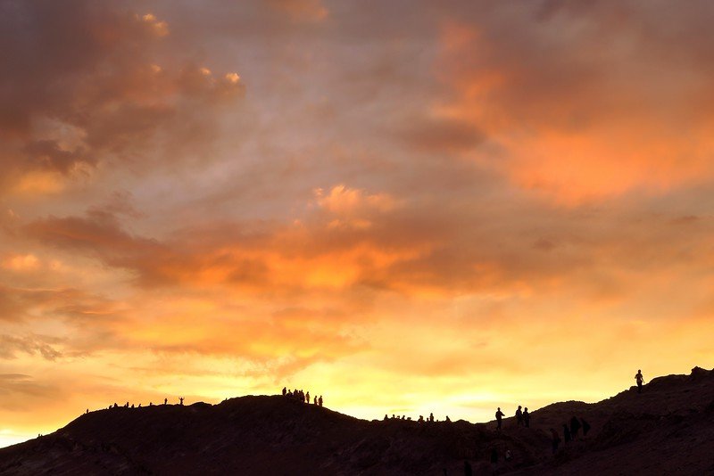 Travelers watching a fiery sunset over Valle de la Luna in the Atacama Desert, Chile, with dramatic golden skies