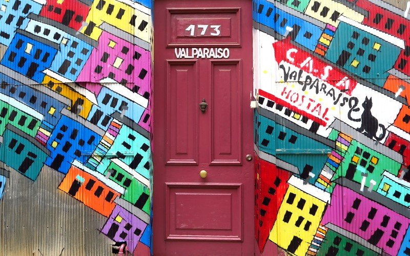 Colorful street art mural of hillside houses surrounding the entrance to Casa Valparaíso Hostel, a vibrant doorway in Chile’s bohemian port city
