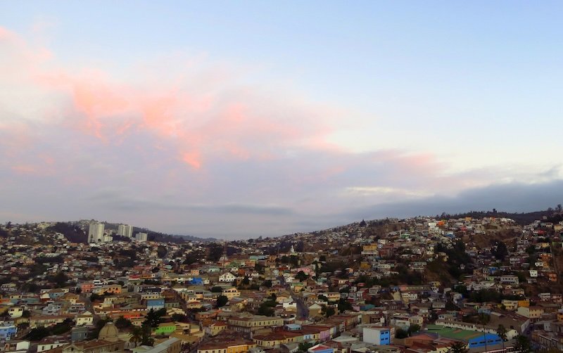 Panoramic view of Valparaíso’s colorful hillside houses at sunset with pastel clouds over Chile’s bohemian port city