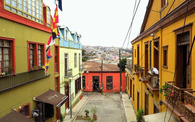 Charming cobblestone street in Valparaíso, Chile, lined with colorful colonial houses painted in green, blue, yellow, and red, showcasing the city’s vibrant bohemian charm and hillside views