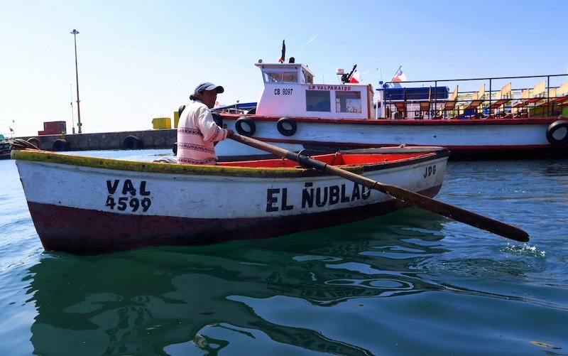 Local fisherman rowing the traditional boat El Nublau in Valparaíso harbor, Chile, with colorful vessels in the background