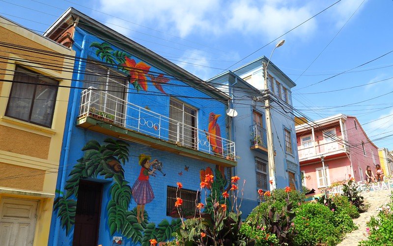Colorful street art mural of a girl with a bird and tropical flowers on a bright blue building in Valparaíso, Chile, a highlight of the city’s vibrant hillside art scene