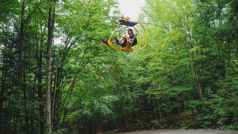 Cyclist That Backpacker Audrey Bergner pedalling high through the forest canopy on the bright yellow Vélo Volant flying bicycle at Au Diable Vert in Sutton, Quebec, experiencing a unique treetop adventure in the Eastern Townships