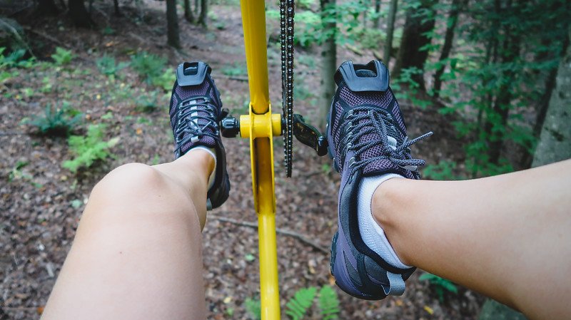 Close-up of legs pedalling the bright yellow Vélo Volant canopy bicycle high above the forest floor at Au Diable Vert in Sutton, Quebec, offering a unique treetop adventure in the Eastern Townships