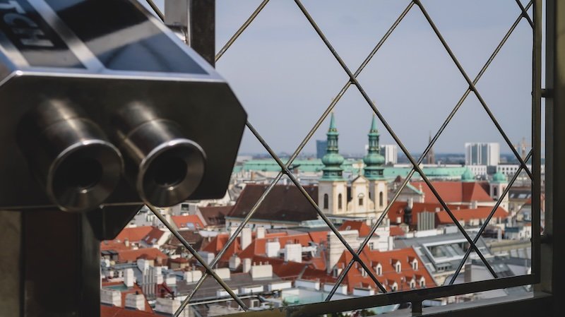 Looking out over the red rooftops and church spires of Vienna, Austria, through a viewing platform atop St. Stephen's Cathedral, with a coin-operated binocular viewer in the foreground and panoramic cityscape beyond Looking out over the red rooftops and church spires of Vienna, Austria, through a viewing platform atop St. Stephen's Cathedral, with a coin-operated binocular viewer in the foreground and panoramic cityscape beyond