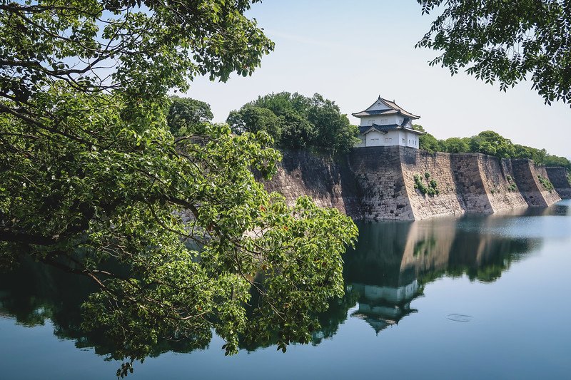 Views of Osaka Castle Park framed beautifully from a distant vantage point by foreground trees and a beautiful moat reflection in Japan