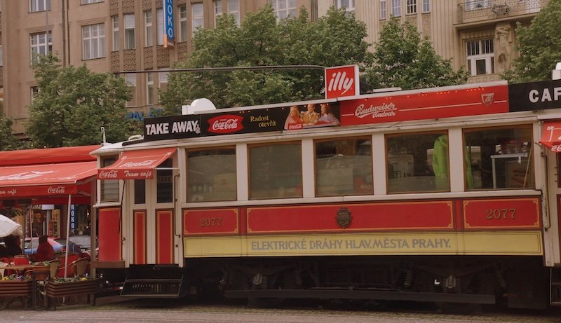 Vintage red and cream Prague Tram converted into a café, parked in a lively city square surrounded by historic buildings in Prague, Czech Republic