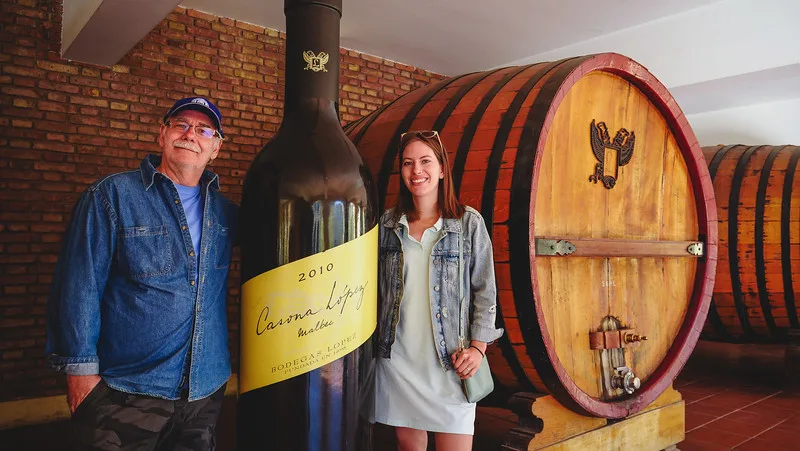 Visiting Bodegas Lopez in Mendoza with Audrey Bergner That Backpacker and Daniel Bergner posing by a giant wine bottle in Argentina