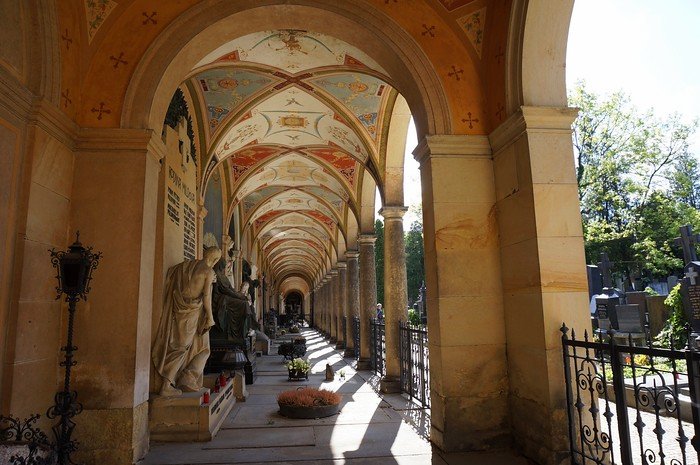 Elegant arched walkway with ornate painted ceilings, statues, and family tombs inside Vyšehrad Cemetery at Vyšehrad fortress in Prague, Czech Republic, illuminated by soft afternoon light