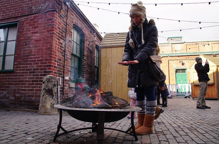 Warming up by the fire in Toronto, Ontario, Canada is a fully bundled up That Backpacker Audrey Bergner dressed for the occasion but with cold hands 