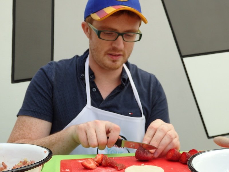 Nomadic Samuel of That Backpacker slicing fresh strawberries during a pierogi cooking class in Warsaw, Poland. As part of the Polish Your Cooking workshop, he learns to prepare traditional dumplings, blending local culture with hands-on food experiences
