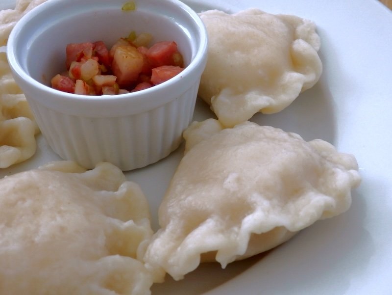 Close-up of traditional Polish pierogi dumplings served in Warsaw, showing delicate handmade dough with crimped edges, accompanied by a small ramekin of diced onions and bacon topping, highlighting Poland’s most iconic comfort food dish