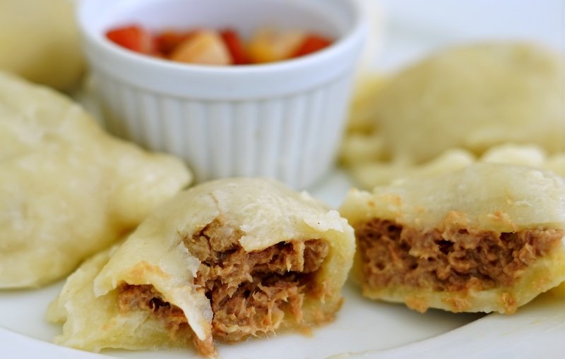 Close-up of traditional Polish pierogi filled with savory meat, showcasing the texture of the dumpling wrapper and rich filling, with a ramekin of vegetables in the background. A must-try dish for foodies exploring Warsaw’s authentic cuisine