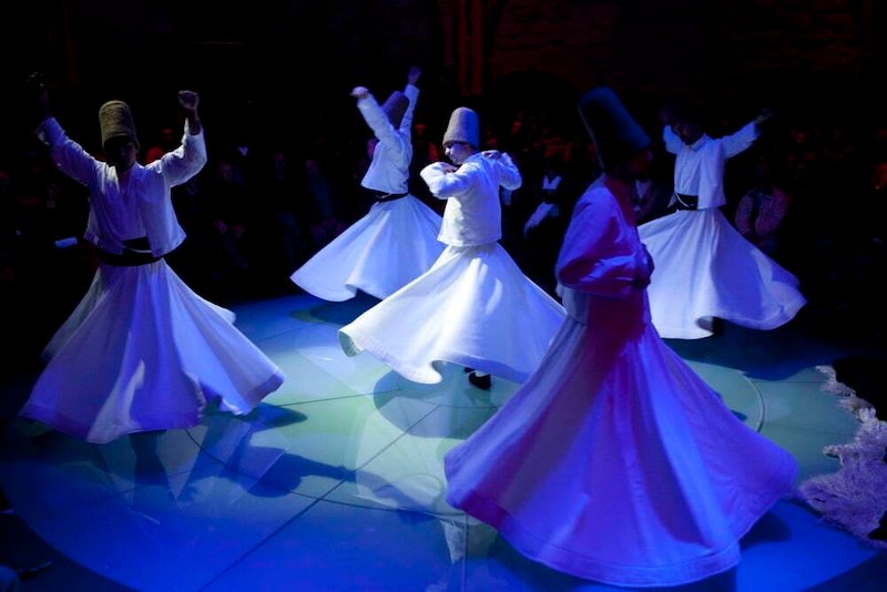 Whirling dervishes Sema Ceremony in Istanbul, Turkey with everyone wearing white robes and performing on stage in unison 