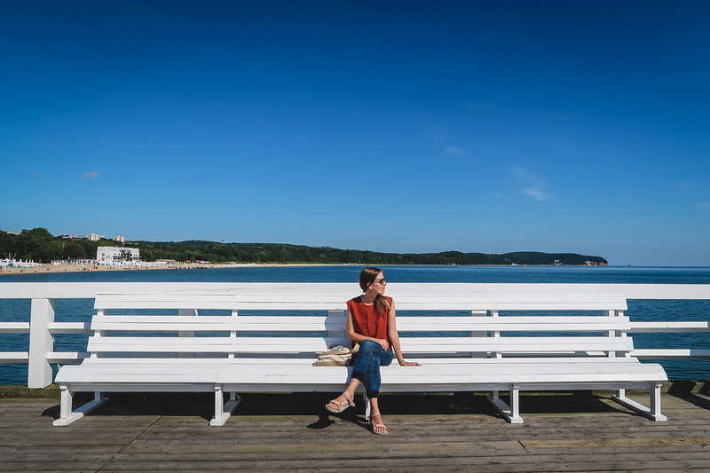 White benches line the length of the Sopot Pier with That Backpacker Audrey Bergner taking a break from it all by sitting down to soak in the charming seaside vibes in Poland