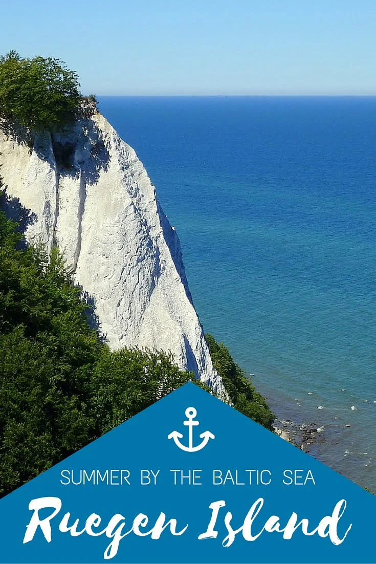 Dramatic white chalk cliffs of Rügen Island rising above the turquoise waters of the Baltic Sea in Germany, framed by lush green forest under a clear blue summer sky