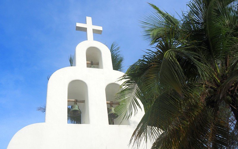 White seaside chapel with bell tower and palm trees in Playa del Carmen, Mexico under a clear blue sky