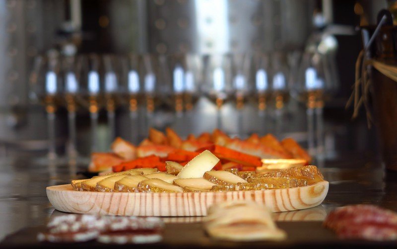 A rustic wine tasting at La Vinyeta winery in Costa Brava, Spain, featuring a delicious spread of artisanal cheeses, cured meats, and bread paired with local wines, offering visitors an authentic culinary experience alongside vineyard views