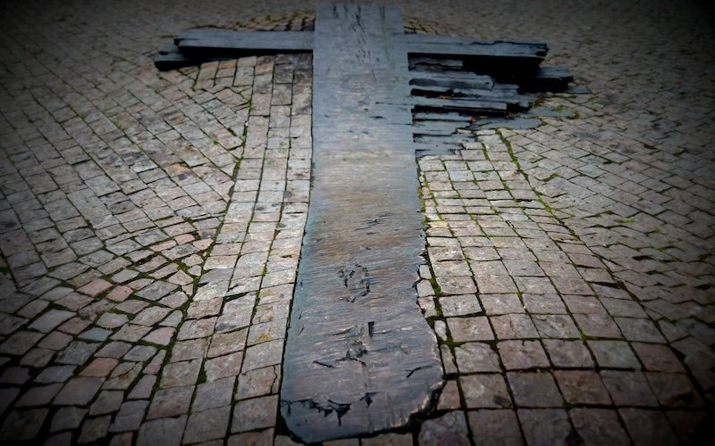 Weathered wooden cross embedded in historic cobblestone pavement in Old Town, Prague, Czech Republic, marking a memorial site along the medieval streets