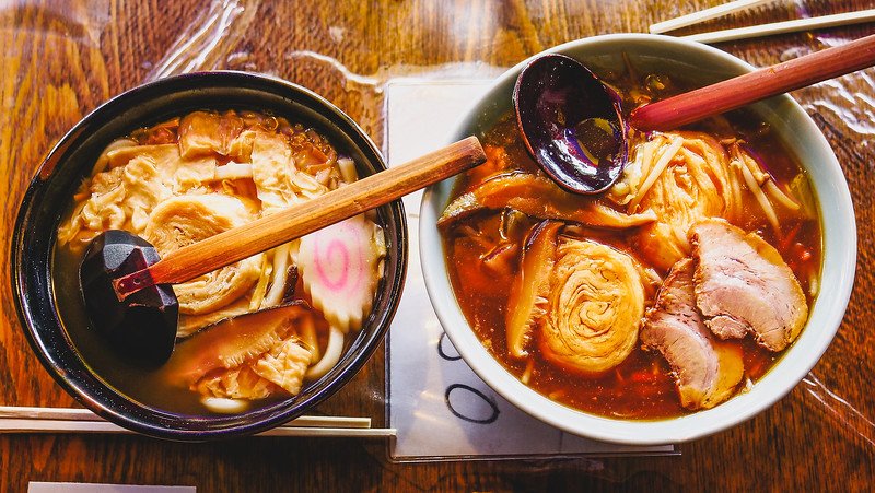 Two steaming bowls of traditional ramen topped with tender yuba (tofu skin), sliced chashu pork, and fish cake served at a local restaurant in Nikko, Japan, showcasing regional cuisine